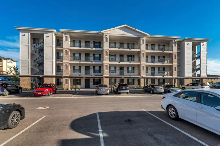 Multi-story apartment building with covered parking, individual unit balconies, exterior stairwells, and a brick and siding facade
