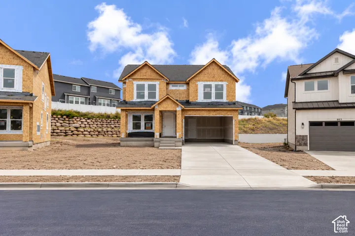 Two-story residential construction featuring a gabled roofline, concrete driveway, attached garage, and multiple window bays