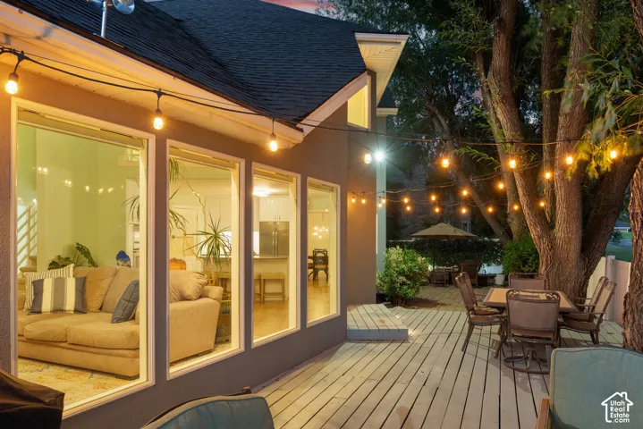 Expansive wood-finish deck with multiple seating areas, mature trees, and large windows providing abundant natural light to interior spaces