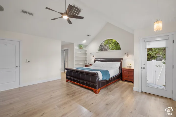 Vaulted ceiling with an exposed beam, wood-finish flooring, built-in shelving, arched window, and a glass-paneled door