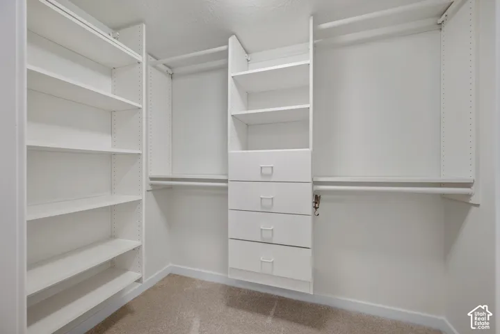 Built-in white shelving system, integrated drawers with metal pulls, multiple hanging rods, and light-colored carpeting