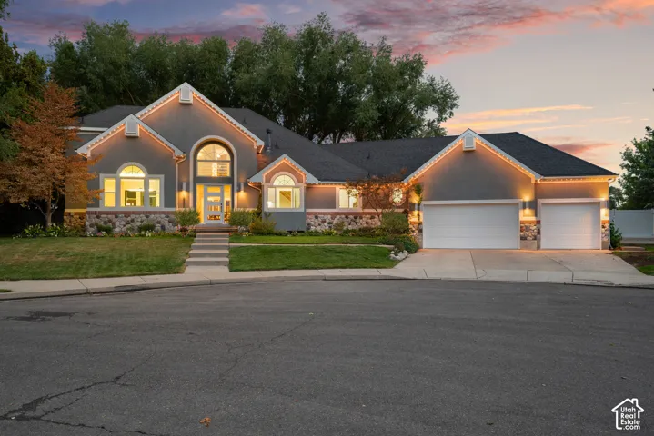 Stucco exterior with stone accents, arched windows, covered entryway, attached two-car garage, and established landscaping