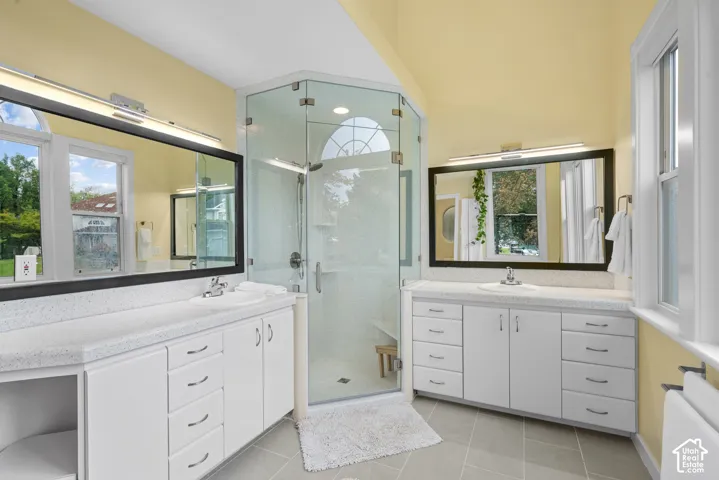 Dual white vanities with integrated sinks, glass-enclosed shower, and tile flooring