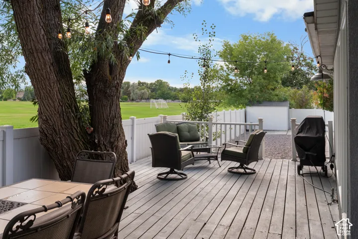 Expansive wood deck with string lighting, mature tree, and white privacy fencing