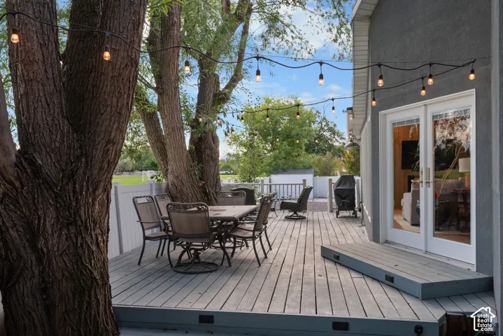 Expansive exterior deck with a wood-finish surface, white privacy fencing, and mature trees providing natural shading