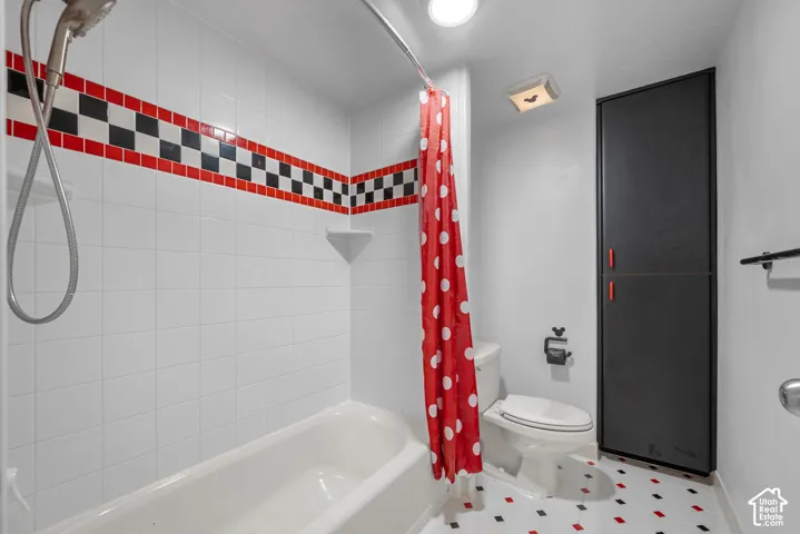 Bathtub with white tile surround, black and red checkered accent tile, and a built-in storage cabinet
