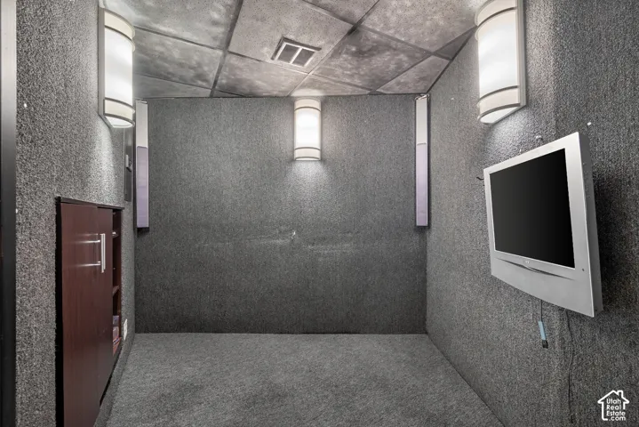 Carpeted room featuring textured wall coverings, integrated wall sconces, ceiling-mounted light, and a built-in wood-finish cabinet