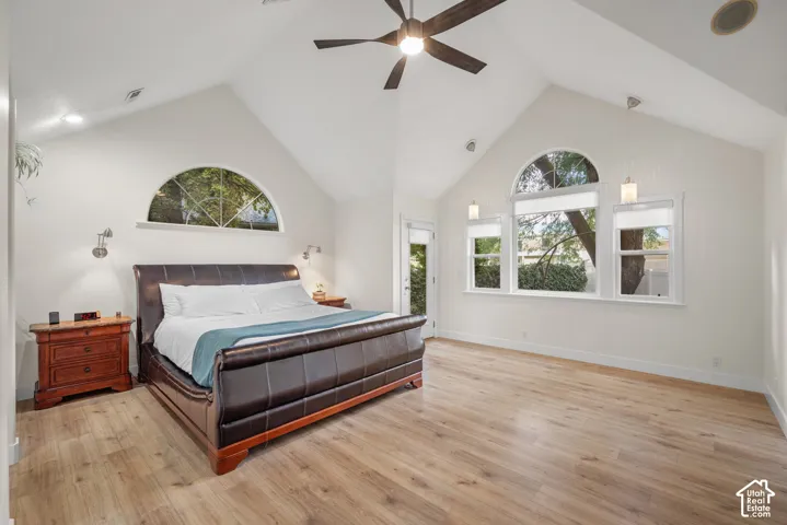Vaulted ceiling with a ceiling fan, wood-finish flooring, half-round transom window, and multiple rectangular windows
