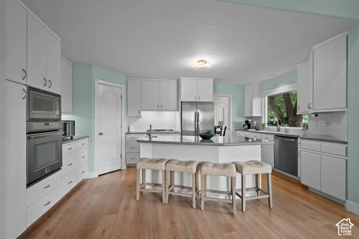 Wood-finish flooring, white cabinetry, stainless steel appliances, central island with seating, and a window above the sink