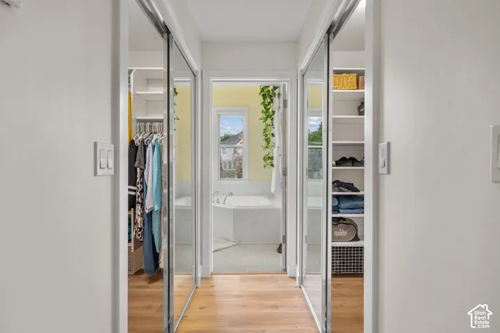 Corridor featuring wood-finish flooring, mirrored sliding doors, and built-in shelving