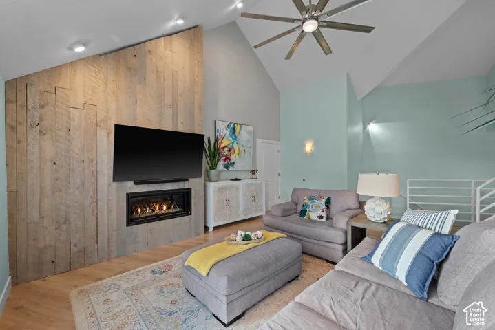 Vaulted ceiling living space featuring a wood-panel accent wall with an integrated fireplace, wood-finish flooring, and a ceiling fan