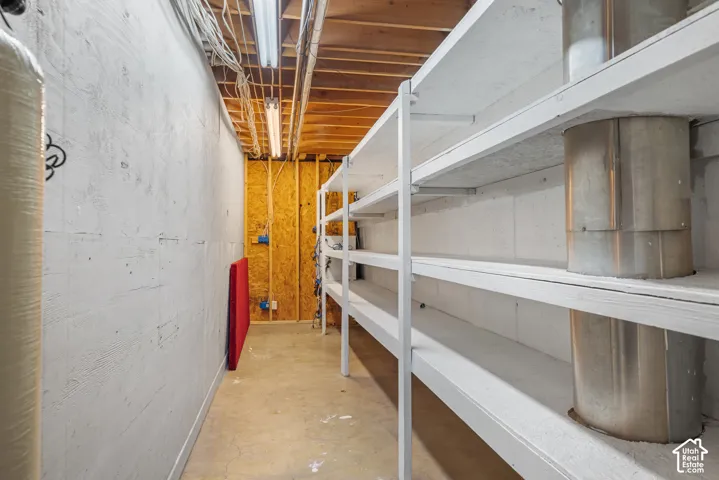 Utility space featuring extensive built-in shelving, exposed ceiling joists, and concrete flooring