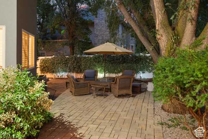 Paver patio with a mature tree, perimeter landscaping, and exterior lighting