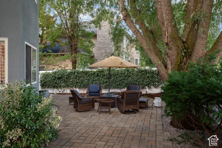 Paved patio with a built-in fire pit, surrounded by mature trees and privacy landscaping