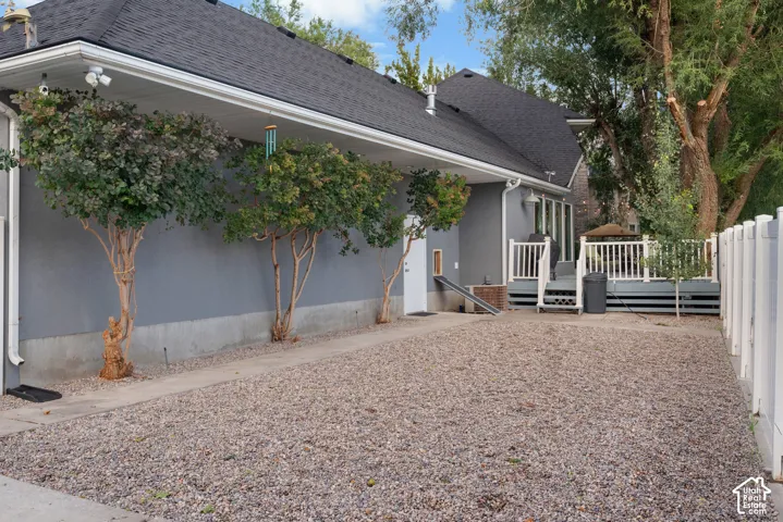 Gravel side yard with a white privacy fence, a raised deck with white railings, and mature trees