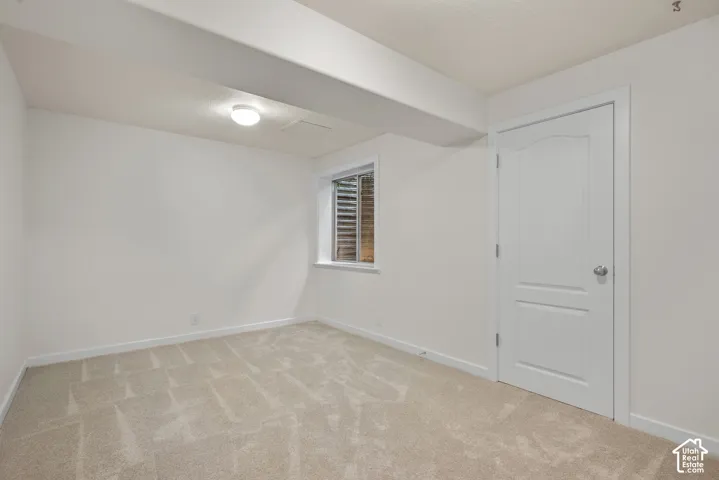 Recessed window with horizontal blinds, overhead flush mount lighting, and light-toned carpeting