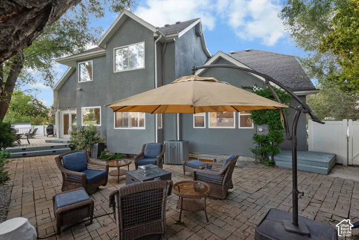 Brick paver patio with a separate multi-level wood deck, stucco exterior, and white window frames