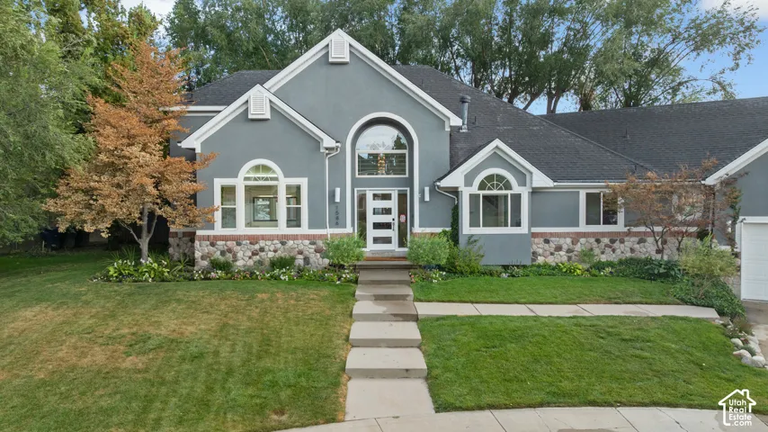 Stucco exterior featuring varied stone veneer accents, arched and rectangular windows, a prominent entryway with an arched transom, and a concrete walk-up