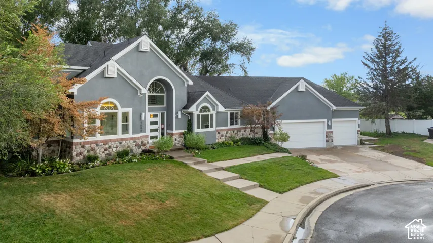Stucco exterior with stone accents, a multi-car garage, arched windows, and a concrete driveway