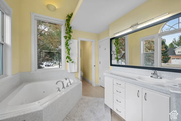 Built-in jetted tub with white surround, double windows, and a vanity with an integrated sink and large mirror