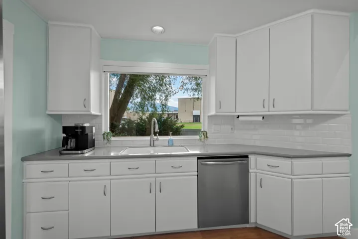 White shaker-style cabinetry, recessed sink, stainless steel dishwasher, white subway tile backsplash, and light-toned countertops