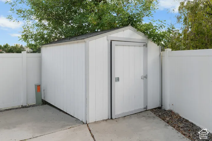 Gable roof storage shed with a panel door, set on a concrete pad, bordered by a white vinyl fence