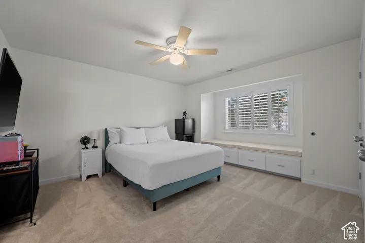 Recessed window with white plantation shutters, built-in window seat with storage drawers, ceiling fan with integrated lighting, and neutral carpet flooring