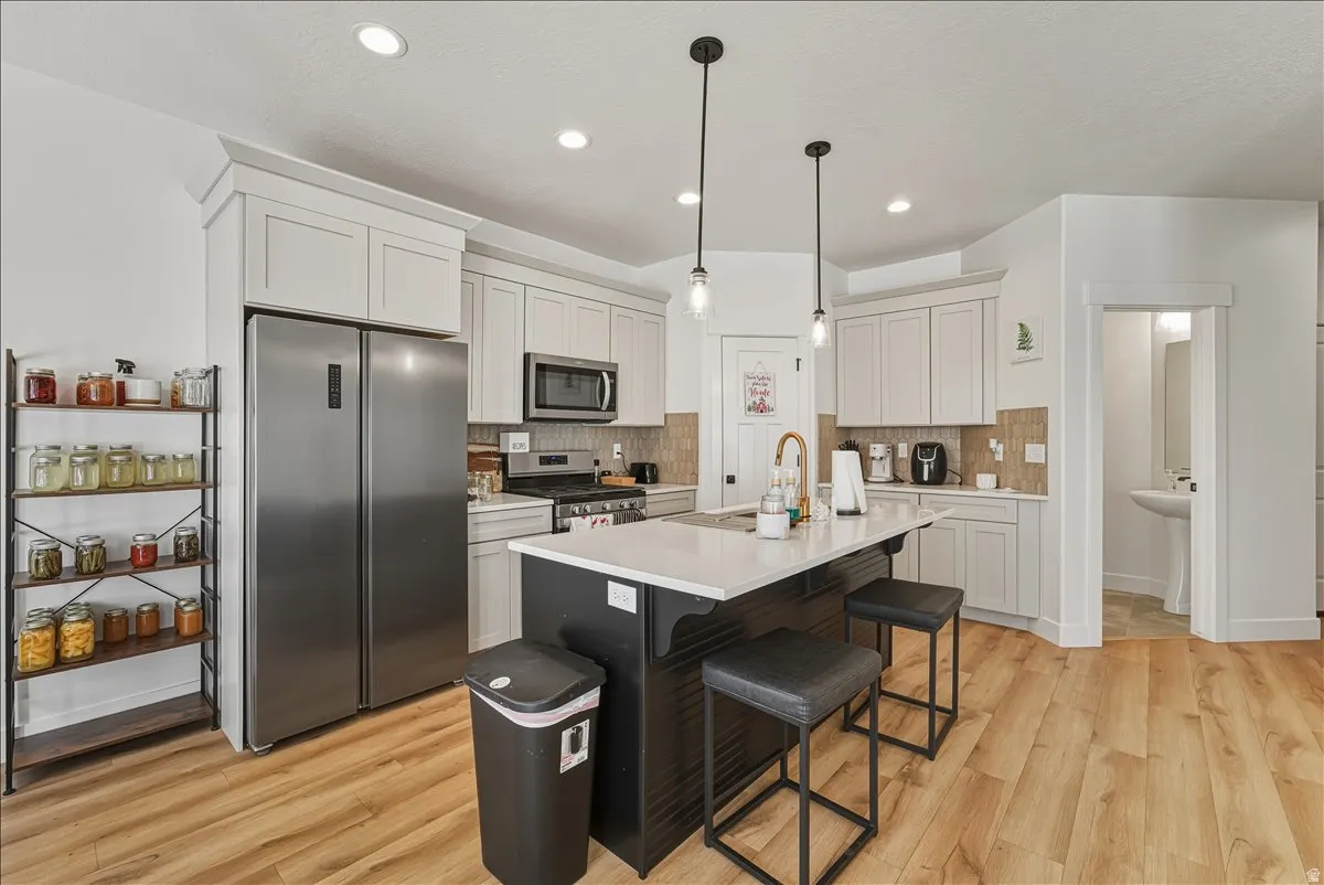 Recessed lighting, wood-finish flooring, white cabinetry, dark kitchen island, and stainless steel appliances