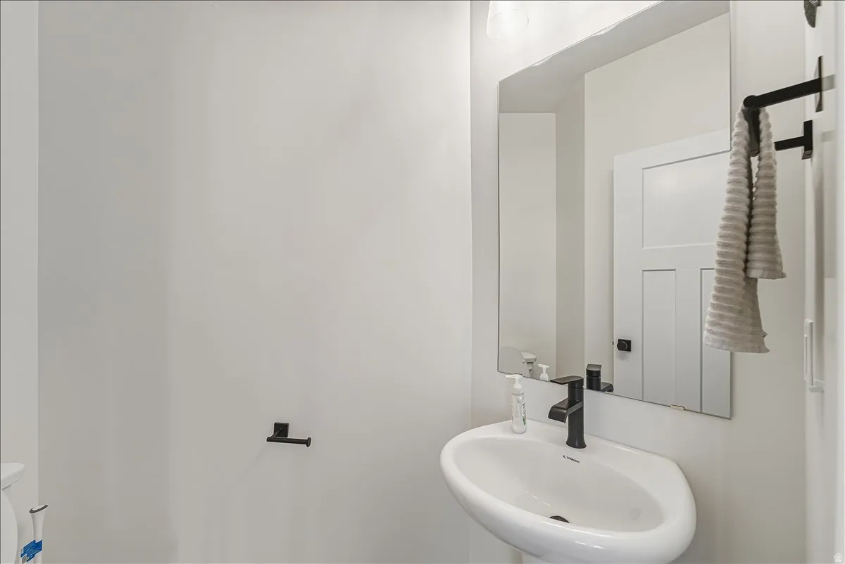 Pedestal sink with a matte black faucet, wall-mounted mirror, and contemporary matte black towel bars