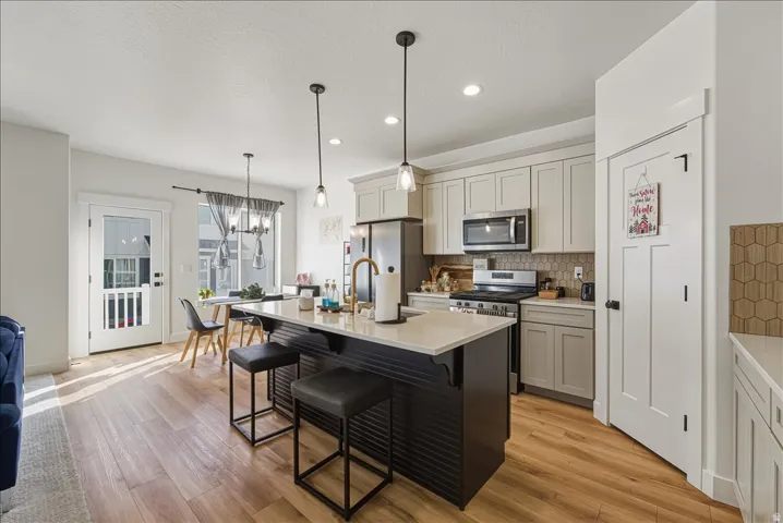 Wood-finish flooring, kitchen island with seating, stainless steel appliances, pendant lighting, and light-colored cabinetry
