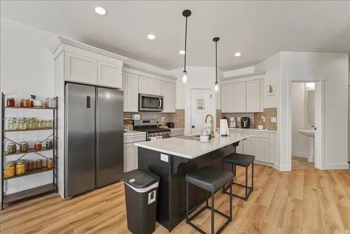 Recessed lighting, wood-finish flooring, white cabinetry, dark kitchen island, and stainless steel appliances