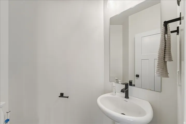 Pedestal sink with a matte black faucet, wall-mounted mirror, and contemporary matte black towel bars