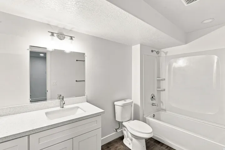 Bathroom featuring a vanity with white cabinetry, a single basin sink, a quartz-finish countertop, a mounted mirror, and a full shower-tub combination