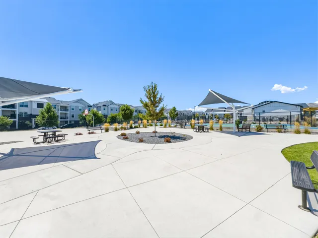 Expansive concrete pathways with integrated shade structures, central landscaping, and surrounding residential buildings