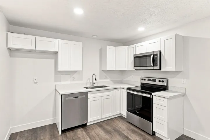 Kitchen featuring white cabinetry, light-toned countertops, stainless steel appliances, and wood-finish flooring