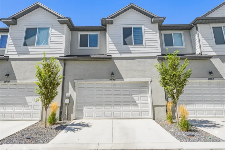 Multi-story townhome with light-colored siding, stucco accents, and an attached garage