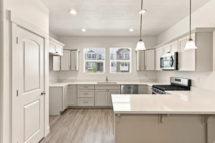 Kitchen featuring light grey cabinetry, stainless steel appliances, light-toned countertops, wood-finish flooring, and recessed lighting