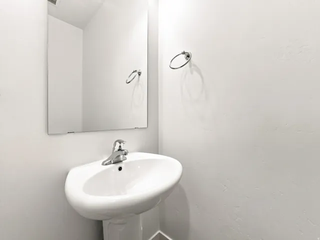 Pedestal sink with a polished chrome faucet, rectangular wall mirror, and a chrome towel ring