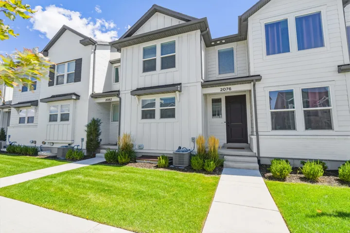 White siding exterior with dark trim accents, concrete walkways, and landscaped shrubbery