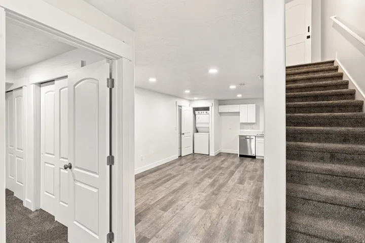 Recessed lighting, wood-finish flooring, white cabinetry, stainless steel dishwasher, and stacked laundry appliances