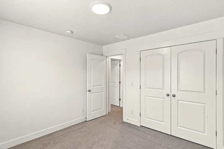 White interior walls, recessed ceiling light, gray carpeting, white paneled doors, and brushed nickel hardware