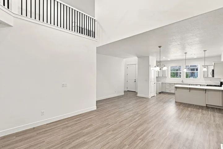 Open-concept living area featuring wood-finish flooring, a two-story ceiling, and a kitchen with pendant lighting, white cabinetry, and a center island