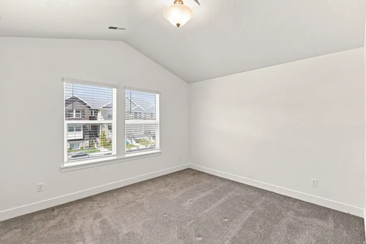 Vaulted ceiling with an attached light fixture, dual windows with blinds, and neutral carpeting