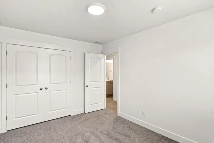 Recessed ceiling light, white painted walls, white trim, two white bi-fold doors with arched panels, and gray carpet flooring