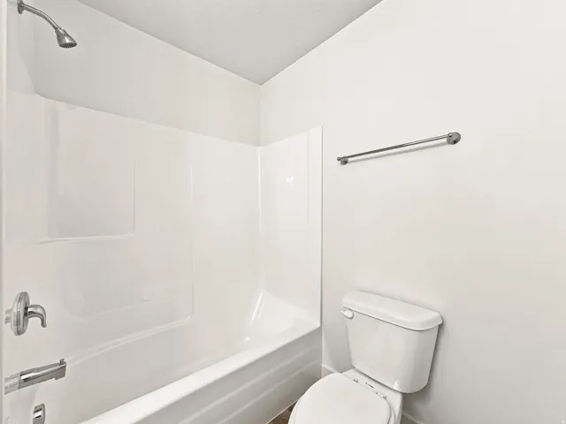 White tub and shower combination with a chrome shower head, chrome faucet, and a wall-mounted toilet