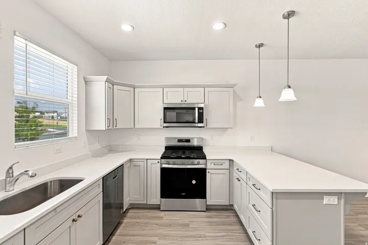 U-shaped kitchen with light-toned cabinetry, light-toned countertops, wood-finish flooring, and stainless steel appliances