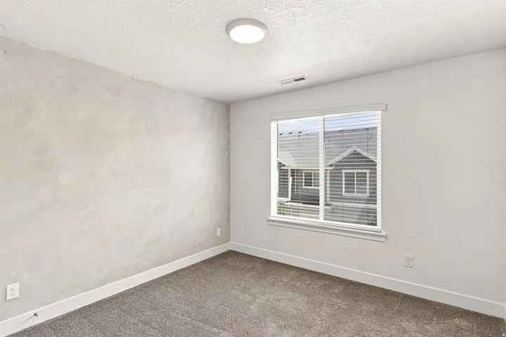 Carpeted flooring, window with blinds, flush mount ceiling light, and a textured accent wall