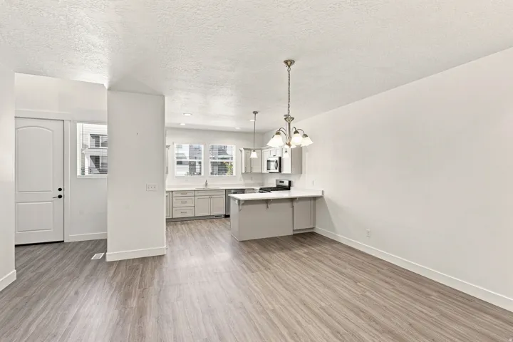 Open concept living area featuring wood-finish flooring, a kitchen with light-colored cabinetry, stainless steel appliances, and a peninsula with countertop seating
