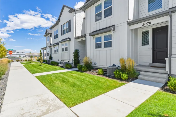 Modern townhome with white siding, dark trim accents, and a landscaped front yard with concrete pathways