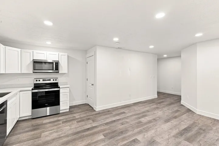 White shaker-style cabinetry, stainless steel appliances, light-toned countertops, recessed lighting, and wood-finish flooring